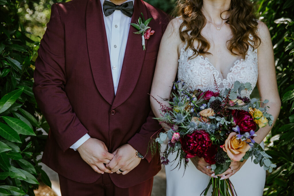 A bride and groom standing next to each other, picturing just their torso and the bride's flower bouquet.