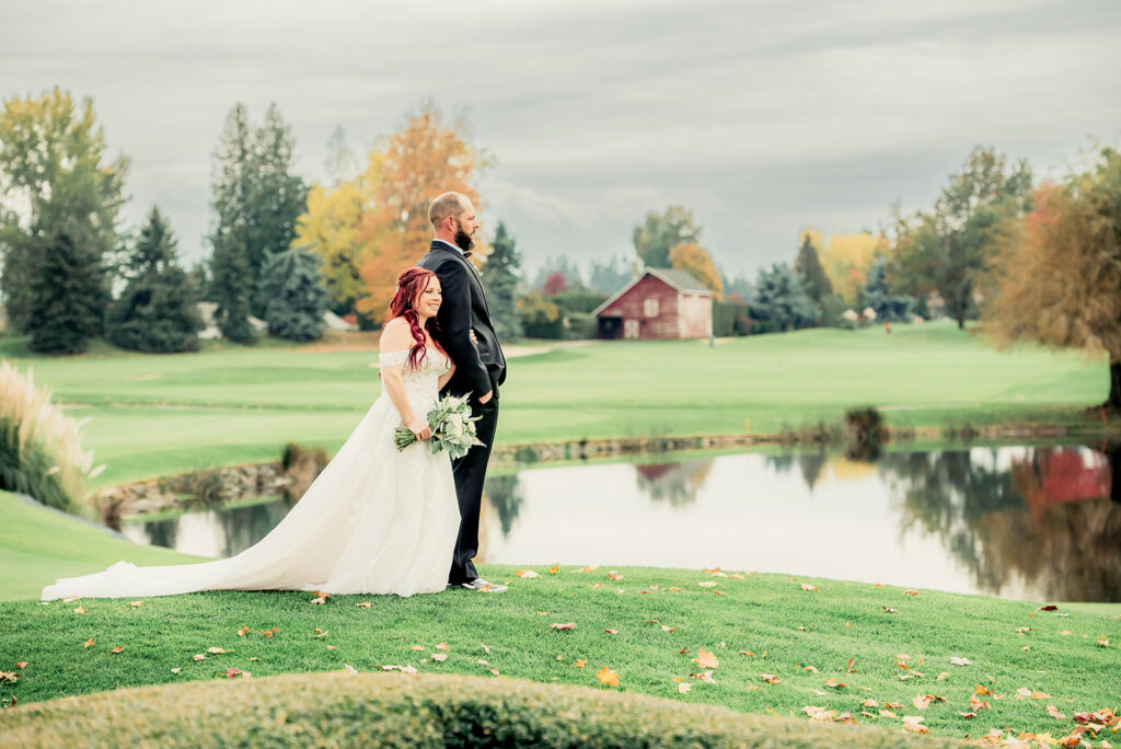 A bride and groom stand arm in arm overlooking a golf course and pond.